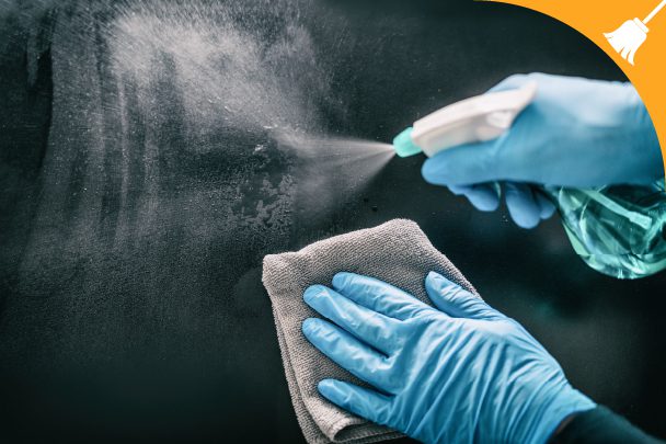 Gloved hands spraying cleaner and wiping a surface with a cloth; cleaning icon in the top right corner.