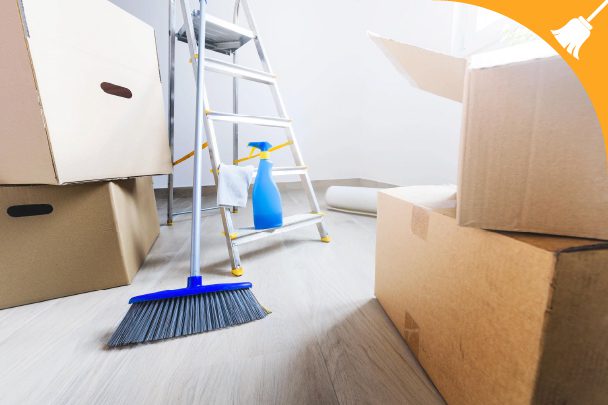 A broom, cleaning spray, and ladder are surrounded by cardboard boxes in a bright room, suggesting cleaning and moving activities.