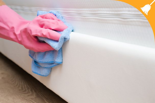 A person wearing pink gloves wipes the side of a white mattress with a blue cloth.