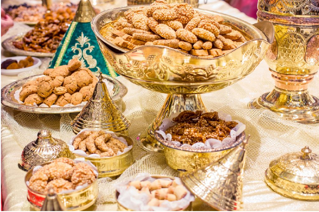 A variety of Moroccan sweets and cookies displayed in ornate gold dishes on a decorated table.