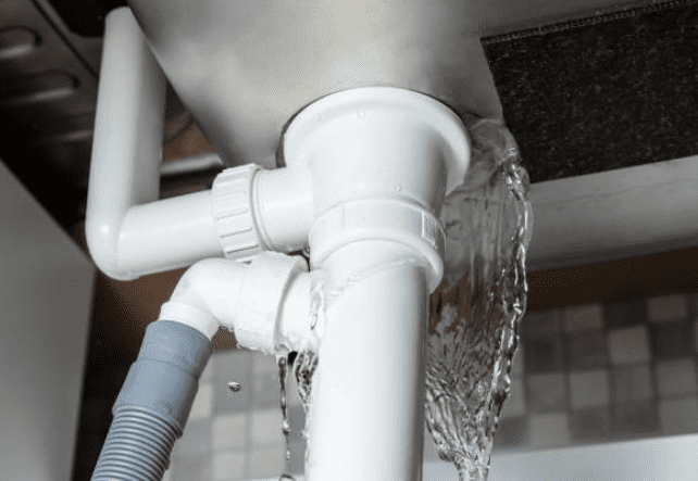 Water is leaking from the white plastic pipe under a sink, indicating a plumbing problem.