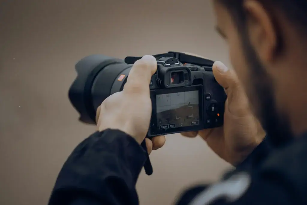 A person holding a digital camera and adjusting settings while looking at the camera's display screen, ready to capture moments from a bustling service de cuisine.
