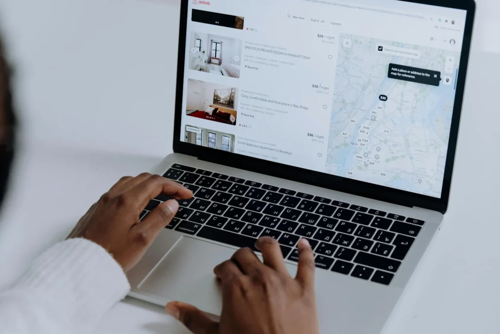 Person using a laptop to browse rental listings with a map and property options, including rentals offering un service de cuisine, displayed on the screen.